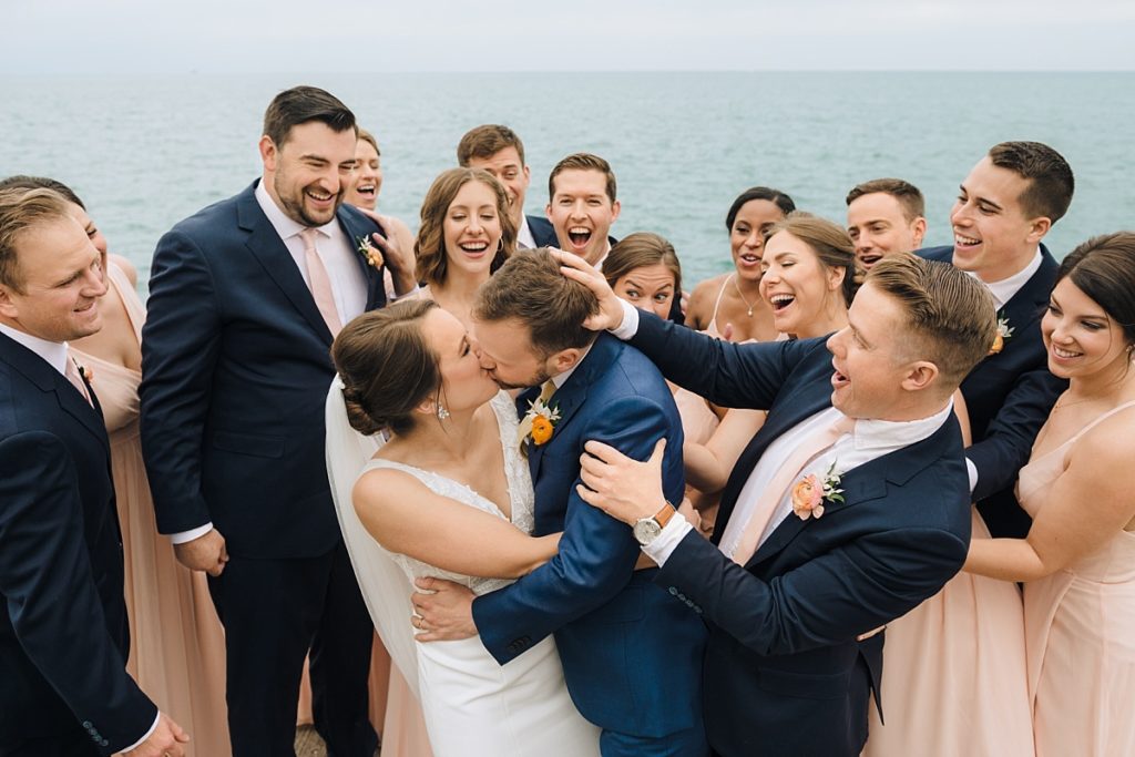 A wedding party goof around at the bride and groom kiss during fun wedding photos in Chicago. 
