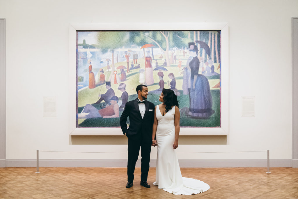 A bride and groom stand together in front of a beautiful piece of art for unique wedding photos at the Art Institute of Chicago.