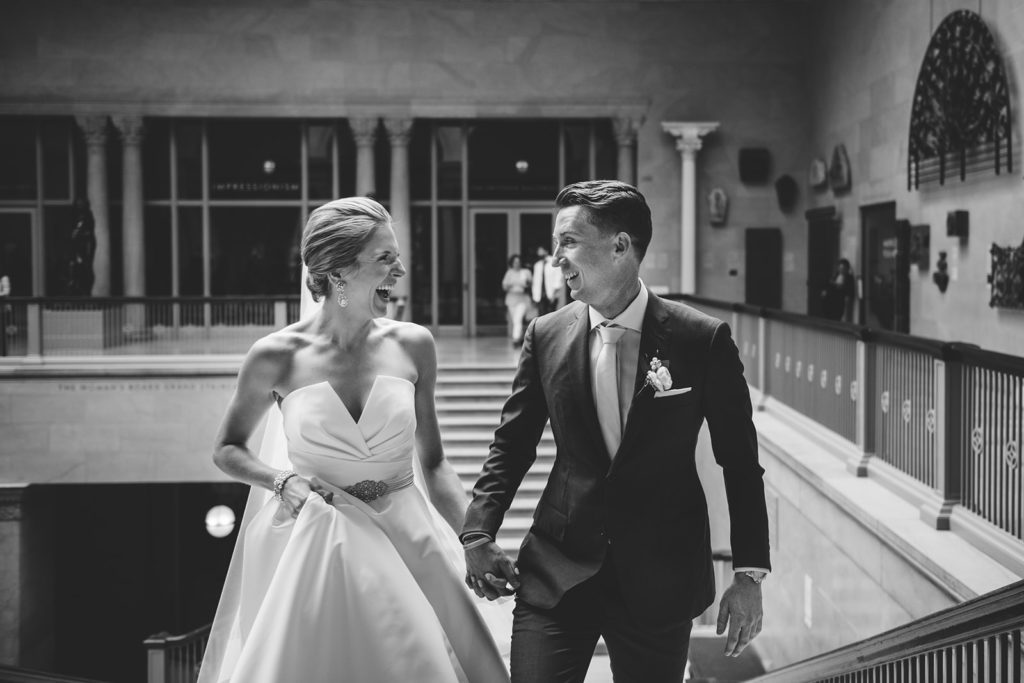 A bride and groom hold hands and laugh together during their wedding at the Chicago Art Institute while the moment is captured by Chicago wedding photographers Ed and Aileen.