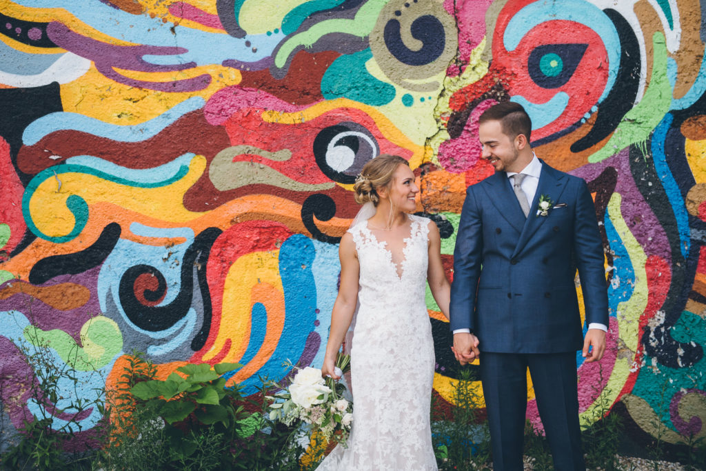 A bride and groom hold hands and smile at each other during a wedding photoshoot in Chicago in front of colorful murals in Pilsen. 