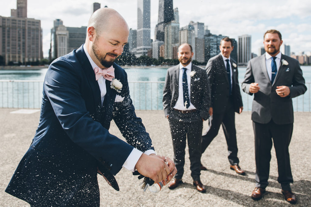 A groom uses his key to shotgun a beer during his wedding photoshoot with Ed and Aileen Photography at Milton Lee Olive Park in Chicago while his groomsmen watch.  